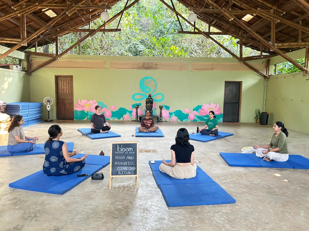 A quiet circle of women in meditation around the Bloom chalkboard sign