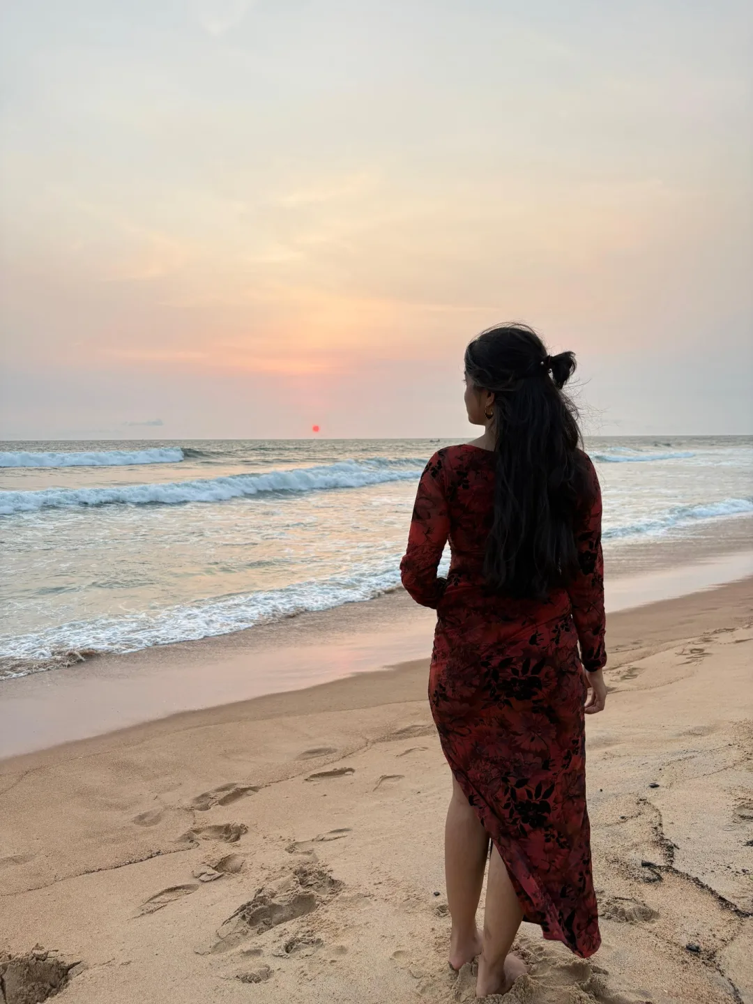 Woman in a red floral dress watching the sunset over the sea